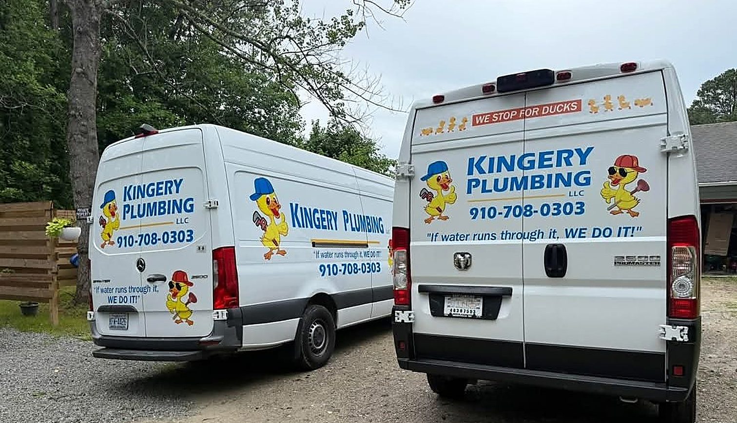 Two Kingery Plumbing service vans parked on a gravel drive, both lettered with the yellow duck mascot and 910-708-0303.